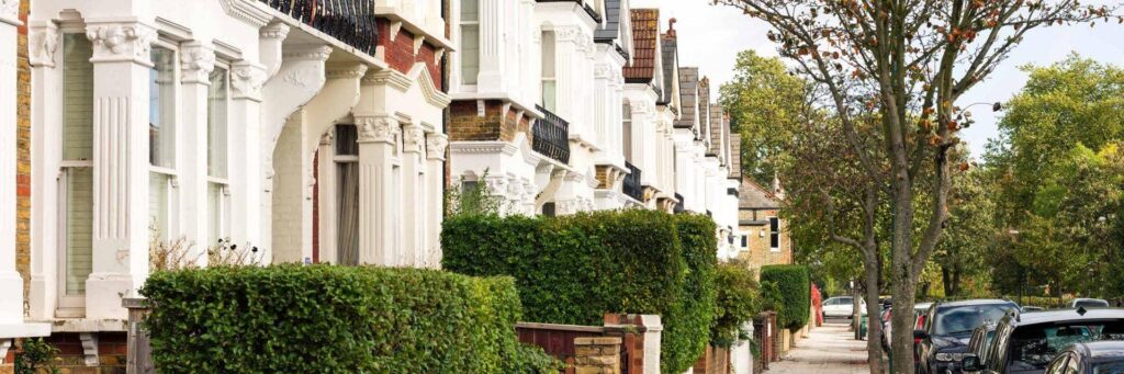 A street view of terraced houses in a nice neighbourhood with trees and hedges outside.